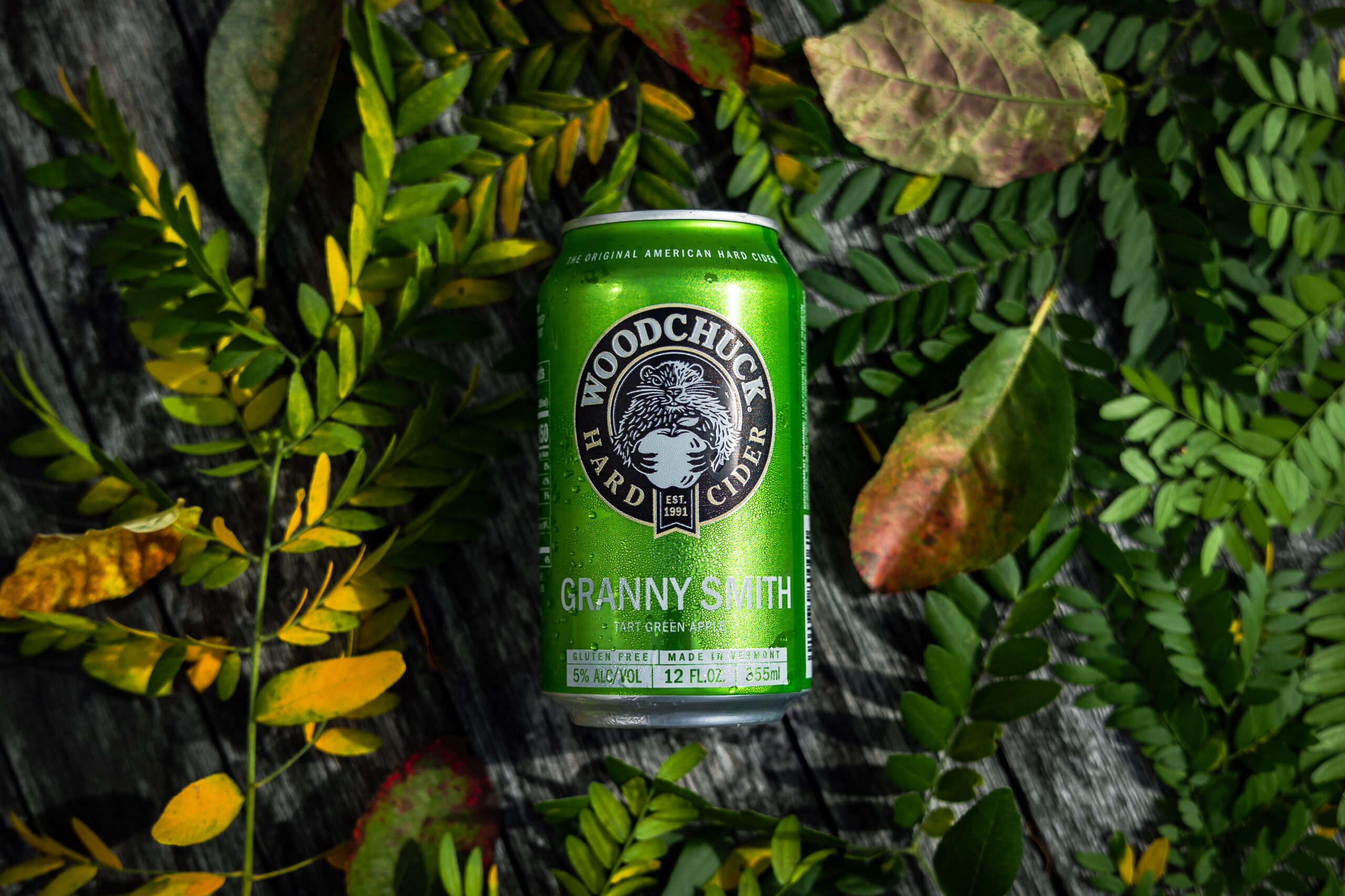 Woodchuck Granny Smith Hard Cider - Tart green apple 12 oz can on top of leaves and greenery