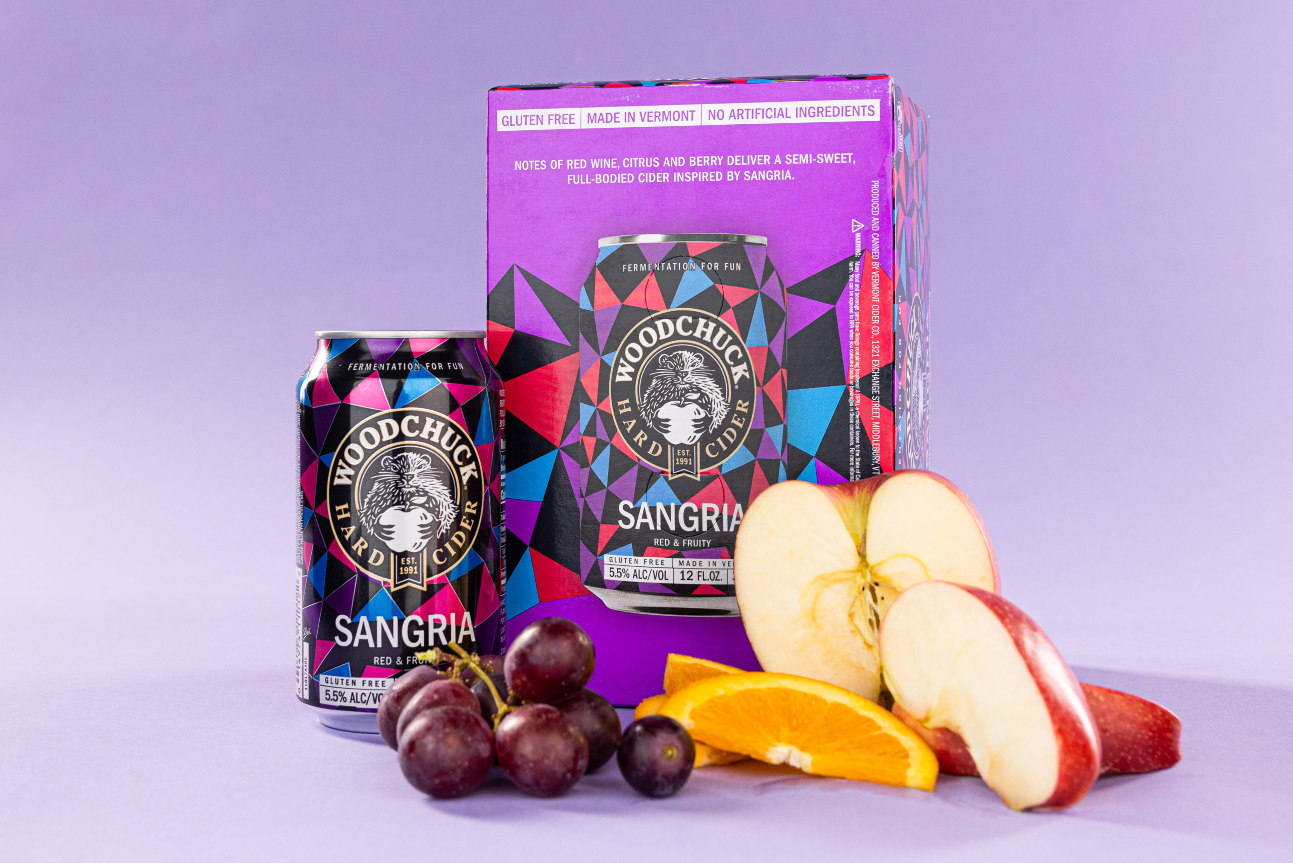 A 12 oz can and a 6 pack of Woodchucks Hard Cider Sangria- red and fruity- with grapes, oranges and apples surrounding the packaging. The 6 pack reads, "Notes of red wine, citrus and berry deliver a semi-sweet, full-bodied cider inspired by sangria"